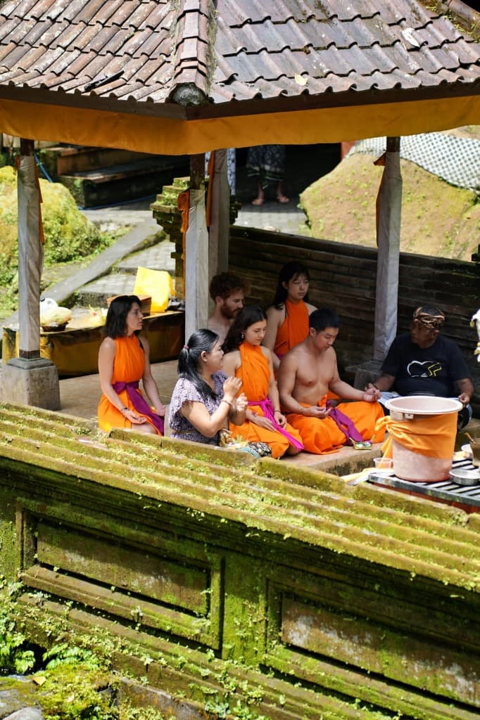 Yoga students sitting for traditional temple purification Melukat water blessing ceremony in Bali