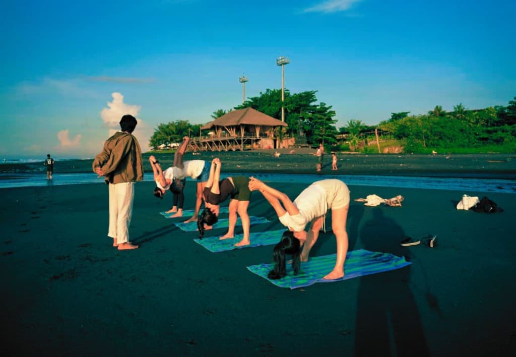 Yoga students practicing alignment poses on a black sand beach in Bali